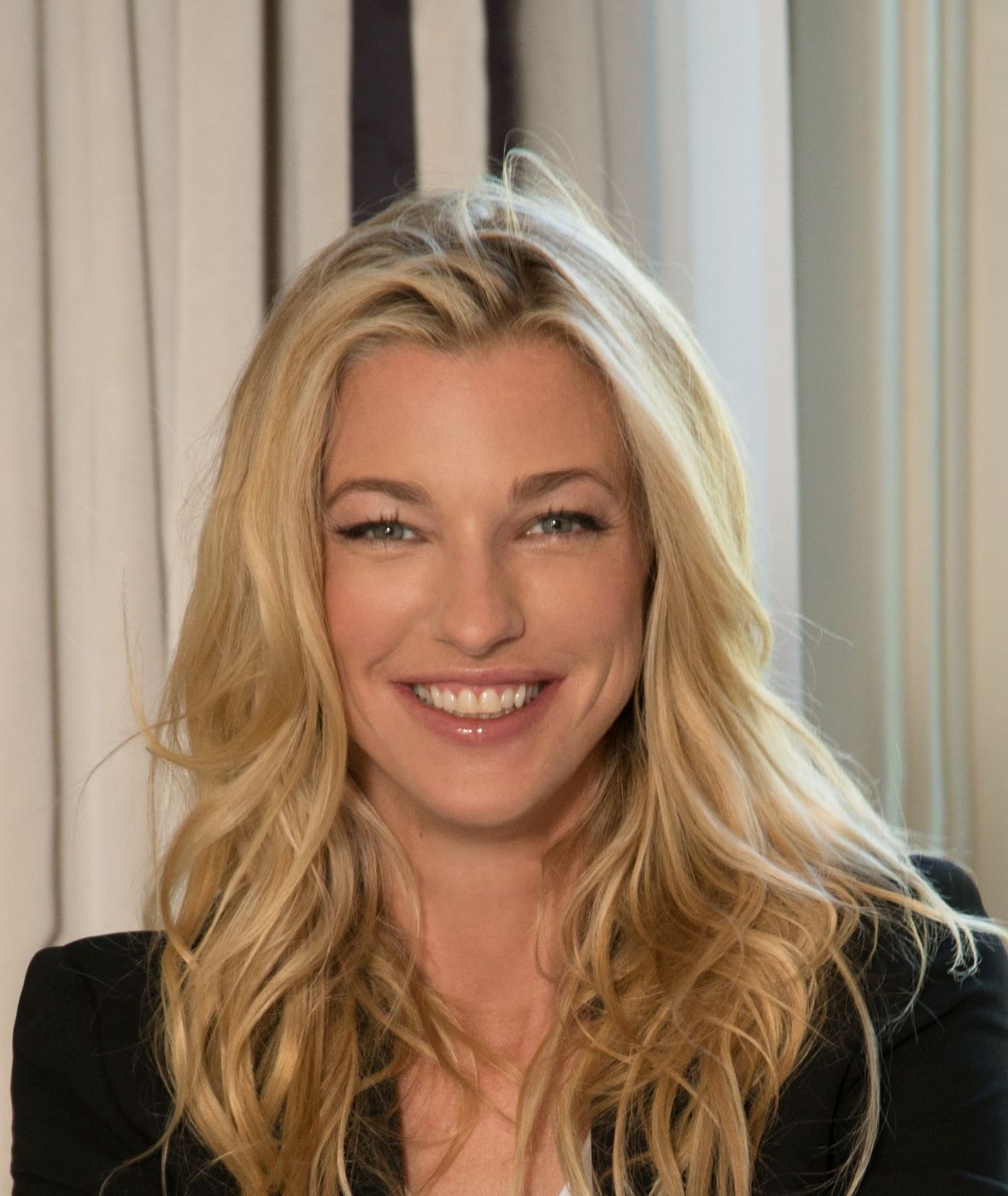 Retrato de Nicole Junkermann sonriendo con calma frente a una cortina clara